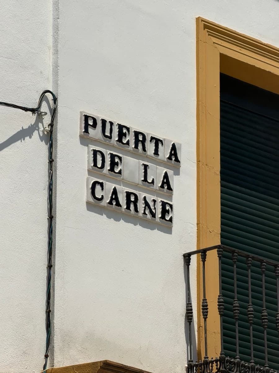 Puerta de la Carne street name painted in black on individual white ceramic tiles