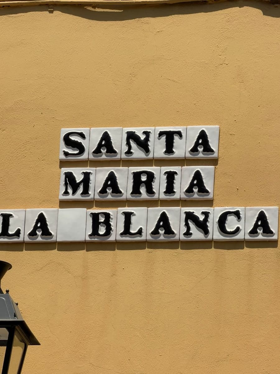 Santa Maria la Blanca street name painted in black on white ceramic tiles against an ochre wall
